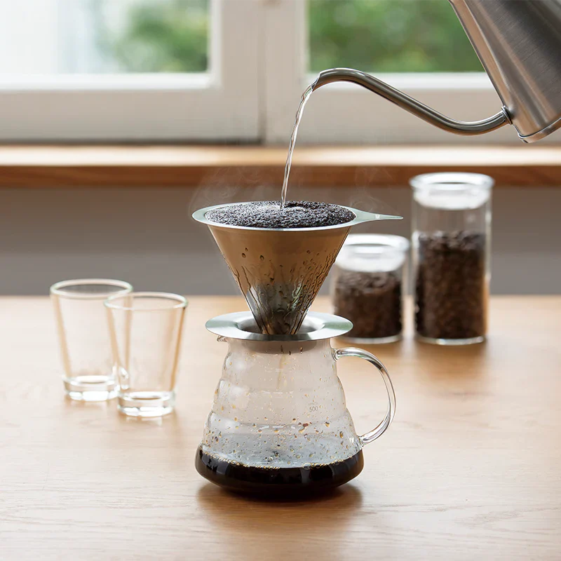 Hario Double Mesh Metal Dripper 01 in use, pouring water over coffee grounds in a stylish kitchen setting.