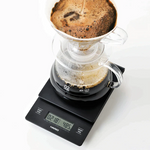 Hario V60 Drip Scale with coffee brewing, matte black design, precise measurement up to 2000g, integrated timer.